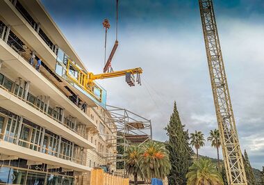 The massive pane is lifted into the building opening using a vacuum suction system and a counterweight traverse