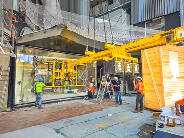 A concave glass pane is precisely positioned and installed beneath a building overhang. Image rights: Heavydrive.com