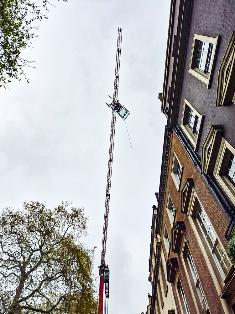 The VSG 750 KRQ vacuum lifting system with glass panel is positioned using a crane.